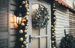 Door of wooden house decorated with festive lights and Chrismas wreath. Holiday house decoration.